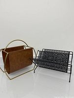 Two magazine racks side by side on white background, one leather/gold-tone metal and one black metal.