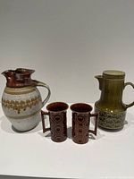 Photo showing the hand-thrown pottery pitcher center, two Portmeirion Jupiter coffee mugs front, and Beswick Zorba coffee pot on right.