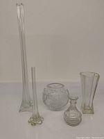 Wide photo showing all five vases together on a white surface against a plain wall