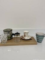 Lot contents arranged on a wooden board: decorative metal box, lucite cubes, Pyrex coffee pot, floral ceramic cup and saucer, and one ceramic pot.