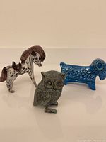 Overall view showing glass horse, ceramic ram, and cast iron owl on white surface