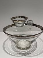 Set of three clear glass bowls with rounded shapes and wide silver trim on edges: large chip bowl, smaller dip bowl, and a divided condiment dish with metal holder.
