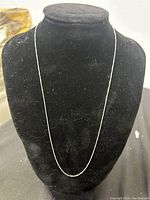 Full view of thin sterling silver necklace displayed on black velvet jewelry bust. Necklace is smooth and fine chain type.