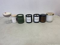Lot view of seven assorted new scented candles with various glass and ceramic containers.