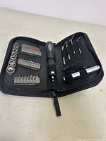 Open tool kit showing multi-bit screwdriver handle, assorted screwdriver bits, socket bits, and bit extension inside green case.