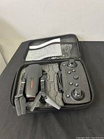 Foldable drone and controller in open carrying case with foam inserts. Drone has folded arms and visible propellers. Controller features buttons and joysticks.
