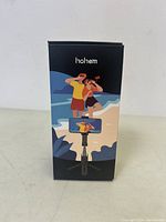 Front view of the Hohem product box showing illustration of couple using selfie stick on beach scene, with Hohem brand name on top.