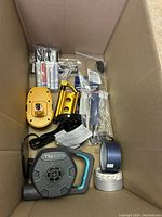 Box containing various hand tools, power tool accessories, adhesive tapes and small hardware parts.