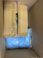 Large cardboard box with items inside, including a blue fabric item wrapped in plastic