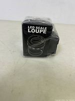 Boxed LED scale loupe wrapped in plastic, showing product illustration and branding details.