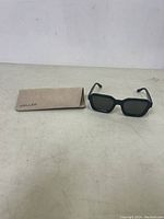 Full view of sunglasses and tan Meller case on flat surface.