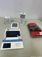 Photo showing a boxed B5 LCD writing tablet, a white travel adapter in a box, and a pair of Fox Racing socks in original packaging on a table.