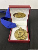 Nikola Tesla commemorative medallion inside red display box, showing front portrait side with blue ribbon attached.