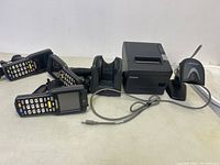 Overview of four handheld mobile barcode scanners with keypads, two charging cradles, Epson receipt printer, and Motorola barcode reader with stand on table.