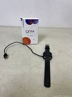 Full view of the QNIX smart watch with charging cable and box in background