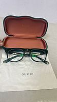 Gucci black eyeglasses inside open green velvet case with brown interior lining and Gucci logo