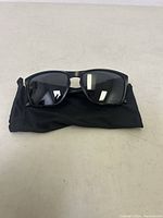 Front view of black Oakley Sylas sunglasses resting on a black soft pouch, showing lens shape and frame details.