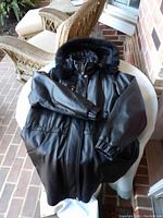 Black leather coat laid on round table, showing full coat, zip front, elastic cuff, and smooth shiny leather surface.