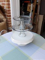 Three cake stands stacked: a white porcelain cake stand at the bottom with a scalloped edge, two clear glass cake stands stacked on top. All in good used condition.