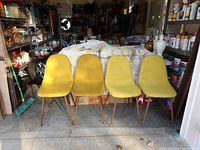 Front view of four yellow cloth covered retro chairs with wooden legs arranged in a row on a garage floor.