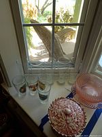 Four pilsner beer glasses on a windowsill, clear glass with colorful brewery logos