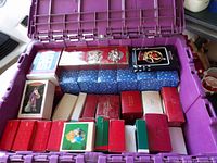 Top view of purple bin filled with many festive ornament boxes, mainly Hallmark, including red, green, white, and blue boxes alongside boxed small face ornaments.