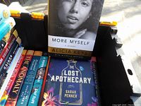 Assortment of hardcover books visible in a plastic crate, showing titles and authors on front covers.