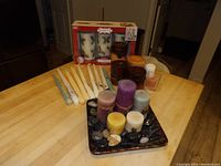 Full display of assorted candles on table including boxed battery Christmas candles, taper candles, pillar candles on tray with stones, and small votive candles