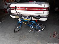 Blue child's racing bike leaning against a car, shows full side profile.