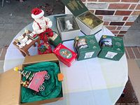 Photo of lot with assorted Christmas figurines, collectibles, mugs, and decorations on a white tablecloth.