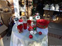 Full lot showing Christmas candle holders, red plaid basket, bells, snowman, and other decorations on a white cloth-covered round table.