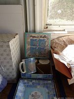 Beach themed dishware box labeled 'Mosaic Shells' including parts of the set inside with one ceramic mug visible with shell decoration.