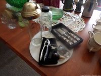Glass drink shaker with brass top and wooden knob, marble board underneath, bottle openers, and wine stopper placed on wooden table.