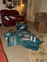 Photo showing Philadelphia Eagles foot locker, fleece blanket, jersey, dartboard, and additional fan items arranged on carpet in living room setting
