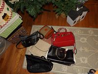 Six assorted ladies handbags arranged on a floor rug near a Christmas tree and decorative items.