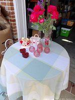 Full lot overview on round table with white and pastel checkered tablecloth, displaying all glass votive holders, heart candle holders, flower pots, and flower vases.
