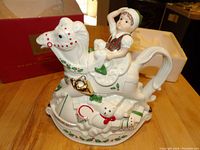 White ceramic rocking horse teapot with elf lid, teddy bear and train base, holly berries decoration, original box in background.