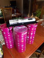 Three pink Lolita cylindrical boxes with cocktail glass illustrations and an electric wine opener placed on top, shown on a wooden table.