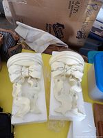 Two cream-colored ribbon-shaped wall shelves with distressed detailing, still in packaging.