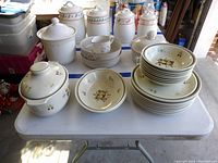 Full set of stoneware dishes displayed on a table showing casseroles, bowls, and plates with fruit and flower motifs.
