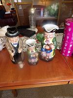 Three Royal Doulton toby jugs arranged on wooden table including Winston Churchill and two colonial character figures.