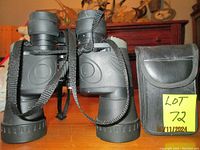 Two black binoculars with neck straps and a black carrying case with flap closure on a wooden table.