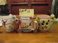 Front view of three vintage ceramic whistle cups showing animal themes and whistle handles with birds.