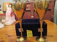 Front view of two brass goblets with velvet box in background on wooden table.