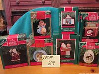 Photo showing all 7 Hallmark ornament boxes arranged on a teal cloth background with a sign marked Lot 29. Boxes feature various Christmas designs and are original packaging.