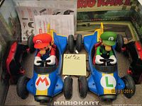 Twin Mario and Luigi RC cars displayed side by side with paperwork behind them and a yellow sticky note labeled 'Lot #22'