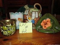 Four items on a wooden surface: Moorcroft vase with floral design, milk glass vase with floral hand-painting, Radford jug with cottage design, brass planter with floral design.