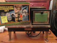 Photo showing the Meccano Microscope Set box and the vintage children's toy stove placed side by side on a wooden floor.