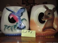 Front view of two ceramic vases/planters showing blue bird on left and deer head on right, each with a hole near center, placed side by side.