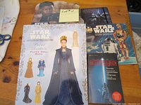 Photo showing Padmé Amidala paper doll book with two sheets of paper dolls, alongside other collectible Star Wars books.